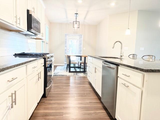 kitchen with stainless steel appliances, wood finished floors, a sink, dark stone counters, and decorative backsplash