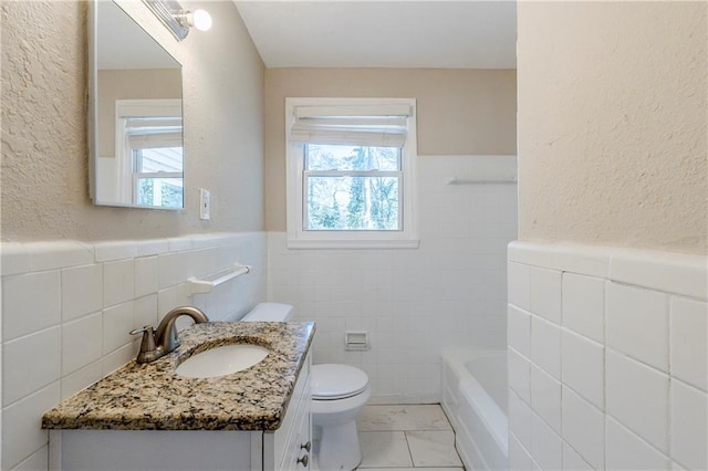 bathroom featuring a wainscoted wall, a washtub, toilet, a textured wall, and tile walls