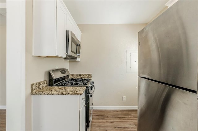 kitchen featuring light stone counters, wood finished floors, appliances with stainless steel finishes, white cabinets, and baseboards