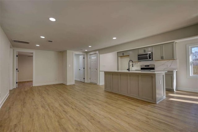 kitchen featuring gray cabinets, dishwasher, sink, a kitchen island with sink, and light wood-type flooring