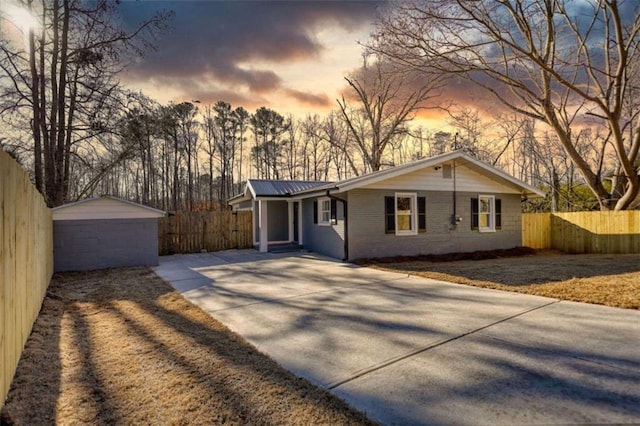 ranch-style house with brick siding, fence, concrete driveway, metal roof, and an outbuilding