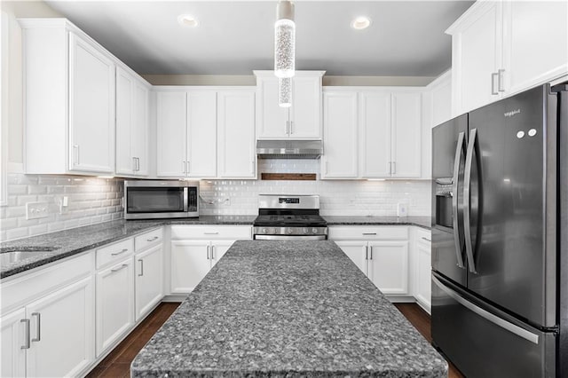 kitchen with under cabinet range hood, stainless steel appliances, dark stone countertops, and a center island