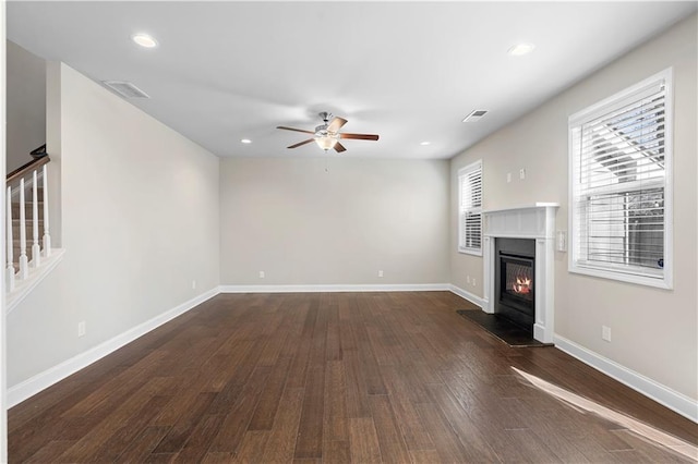 unfurnished living room with baseboards, visible vents, a glass covered fireplace, stairway, and dark wood-style flooring