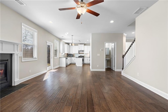 unfurnished living room featuring dark wood-style flooring, visible vents, baseboards, stairway, and a glass covered fireplace