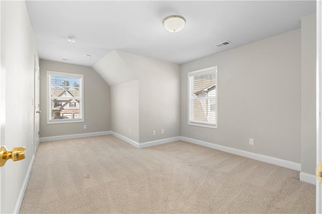 additional living space with light carpet, vaulted ceiling, visible vents, and baseboards