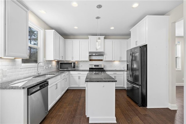 kitchen with a kitchen island, dark stone countertops, hanging light fixtures, stainless steel appliances, and a sink