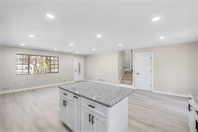 kitchen with a kitchen island, light stone countertops, white cabinets, and light wood-type flooring