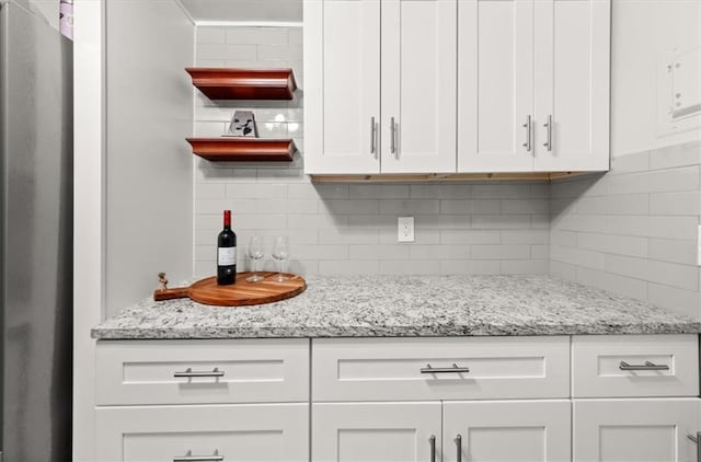 kitchen featuring backsplash, stainless steel fridge, white cabinets, and light stone counters