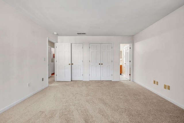 unfurnished bedroom featuring carpet, baseboards, visible vents, multiple closets, and connected bathroom