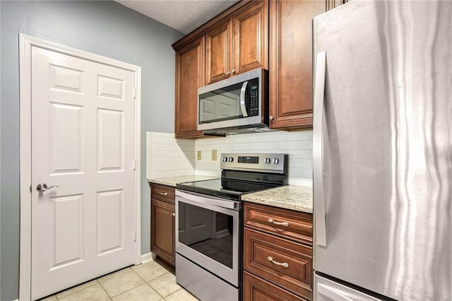 kitchen with light tile patterned flooring, appliances with stainless steel finishes, tasteful backsplash, light stone countertops, and a textured ceiling