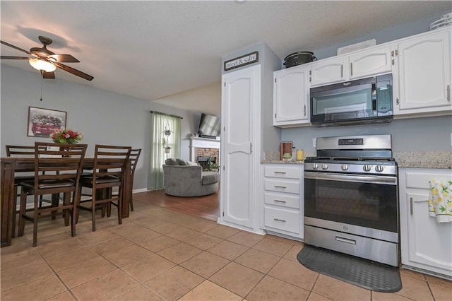 kitchen featuring black microwave, a stone fireplace, ceiling fan, stainless steel range with gas cooktop, and light tile patterned floors