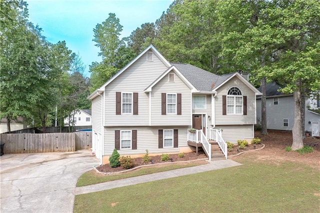 split foyer home featuring fence, a chimney, concrete driveway, and a front yard