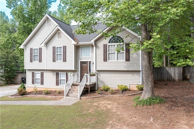 bi-level home with fence, a shingled roof, and a front yard