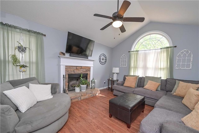 living area featuring a ceiling fan, vaulted ceiling, a stone fireplace, and wood finished floors