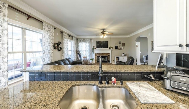 kitchen with light stone counters, a fireplace, a sink, white cabinetry, and ornamental molding