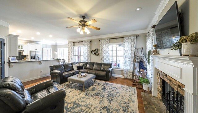 living room featuring ceiling fan, a fireplace, baseboards, ornamental molding, and dark wood finished floors