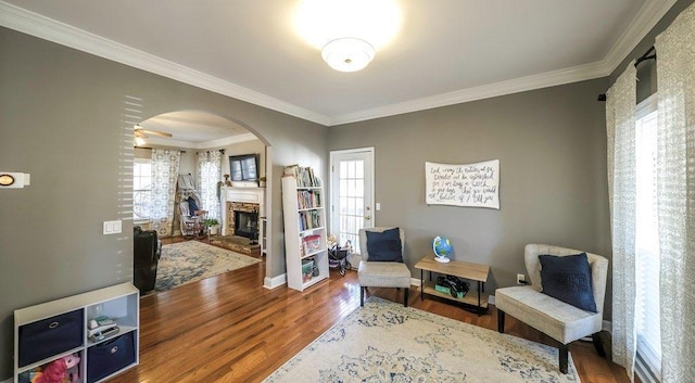 sitting room featuring plenty of natural light, crown molding, arched walkways, and wood finished floors