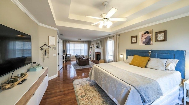 bedroom featuring dark wood-type flooring, a tray ceiling, a brick fireplace, and crown molding
