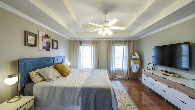 bedroom with crown molding, a tray ceiling, dark wood finished floors, and a ceiling fan