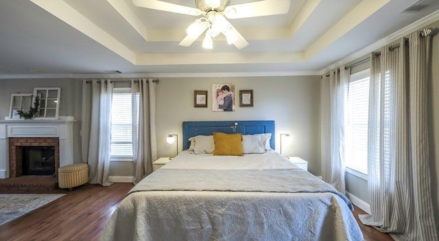 bedroom with dark wood-style floors, multiple windows, and a tray ceiling
