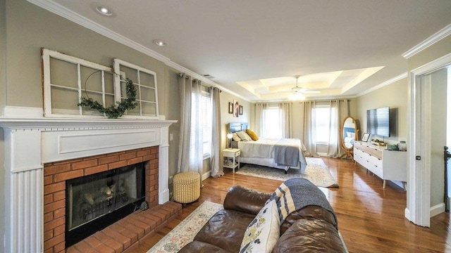 bedroom with wood finished floors, visible vents, ornamental molding, a brick fireplace, and a tray ceiling