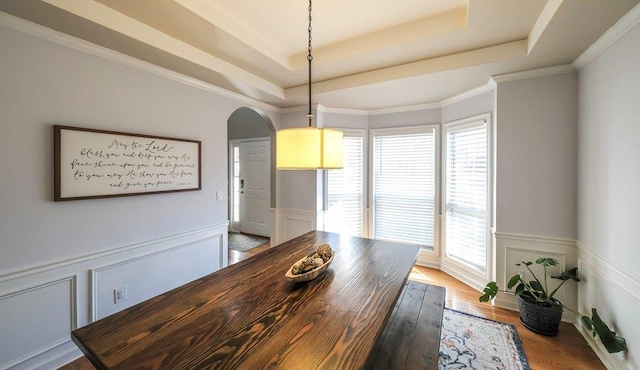 dining space with plenty of natural light, arched walkways, a raised ceiling, and wood finished floors