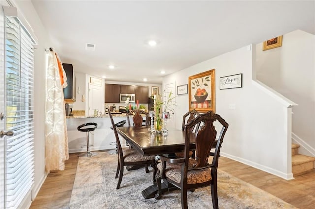 dining space with baseboards, visible vents, stairway, and light wood finished floors