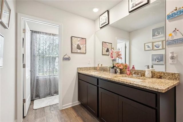 bathroom featuring double vanity, baseboards, a sink, and wood finished floors