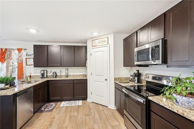 kitchen featuring a breakfast bar area, light wood finished floors, stainless steel appliances, dark brown cabinetry, and a sink