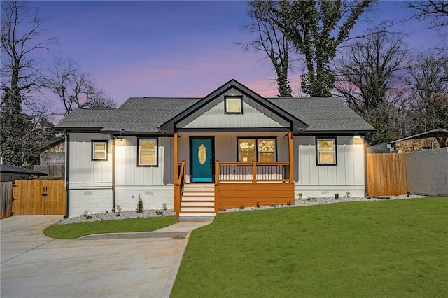 modern farmhouse with board and batten siding, roof with shingles, covered porch, a lawn, and a gate