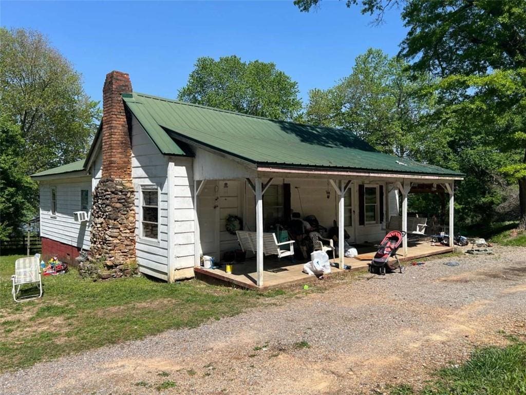 view of side of property with a chimney, metal roof, and a porch