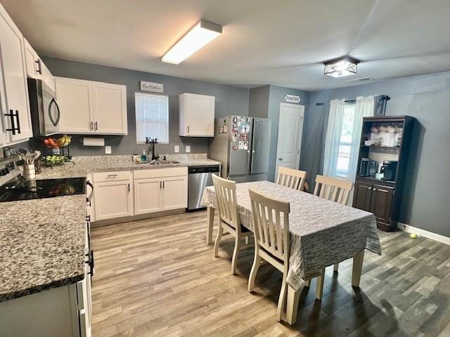 kitchen with light hardwood / wood-style floors, sink, light stone counters, appliances with stainless steel finishes, and white cabinets