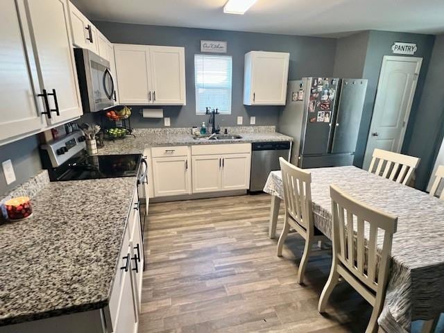 kitchen with stainless steel appliances, light hardwood / wood-style floors, white cabinets, sink, and light stone countertops