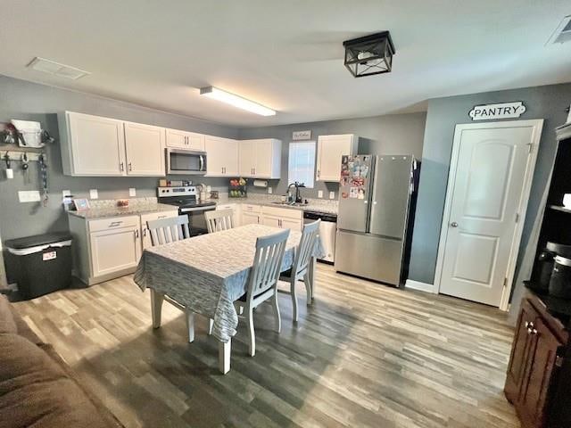 kitchen with appliances with stainless steel finishes, sink, light hardwood / wood-style floors, and white cabinets