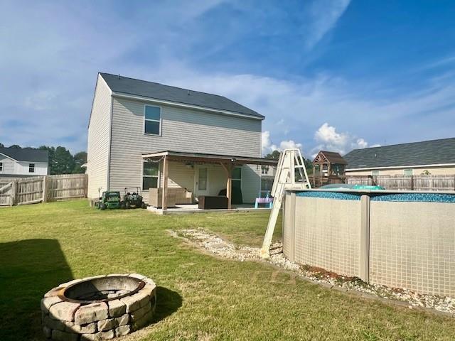 back of house featuring a fire pit, a lawn, a patio, and a fenced in pool