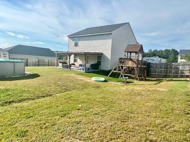 rear view of property featuring a fenced in pool, a playground, and a lawn