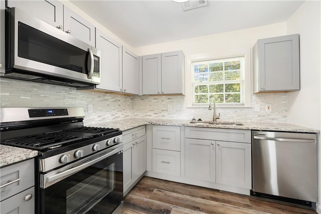 kitchen with gray cabinetry, backsplash, sink, appliances with stainless steel finishes, and dark hardwood / wood-style flooring