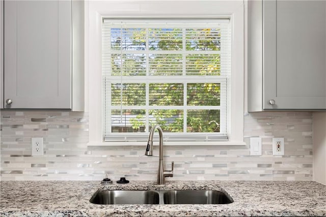 kitchen with tasteful backsplash, light stone counters, sink, and white cabinets