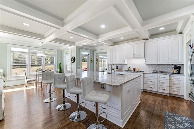 kitchen with light stone counters, dark hardwood / wood-style flooring, a center island with sink, and white cabinets