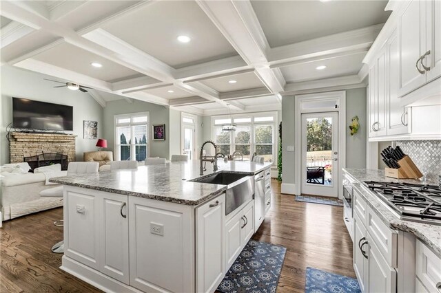 kitchen featuring dark hardwood / wood-style floors, an island with sink, sink, light stone countertops, and white cabinets