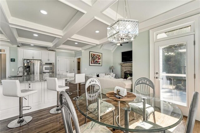 dining space featuring a brick fireplace, coffered ceiling, beamed ceiling, an inviting chandelier, and dark hardwood / wood-style floors