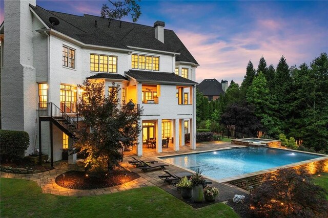 15910 Meadow King Way, Milton, GA 30004 - back of house at dusk with a chimney, a patio, stairway, a pool with connected hot tub, and a lawn