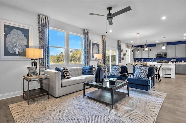 living room featuring a ceiling fan, light wood finished floors, recessed lighting, and baseboards