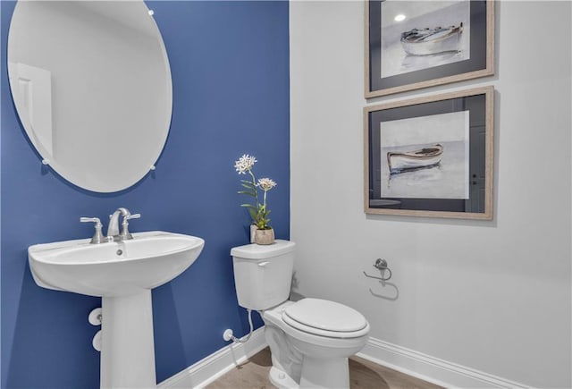 half bath with baseboards, toilet, and wood finished floors