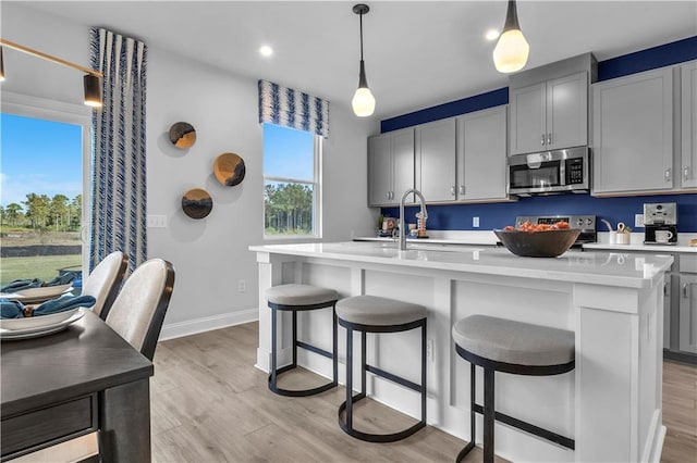 kitchen with appliances with stainless steel finishes, light wood-style floors, an island with sink, a sink, and light countertops