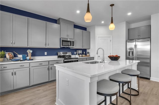 kitchen featuring stainless steel appliances, a sink, gray cabinetry, a breakfast bar, and light wood-style flooring