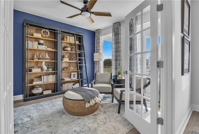 living area featuring baseboards, ceiling fan, and wood finished floors