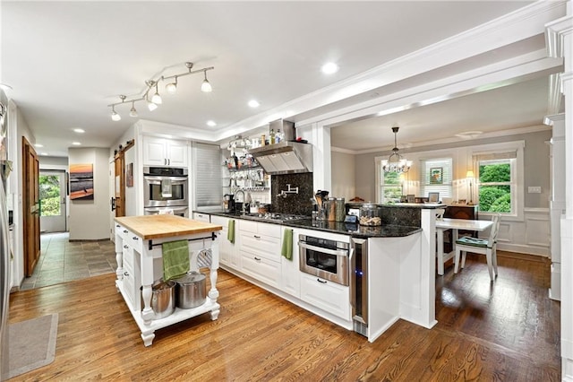 1438 Salem Dr, Alpharetta, GA 30009 - kitchen featuring wooden counters, crown molding, wall chimney range hood, white cabinets, and healthy amount of natural light