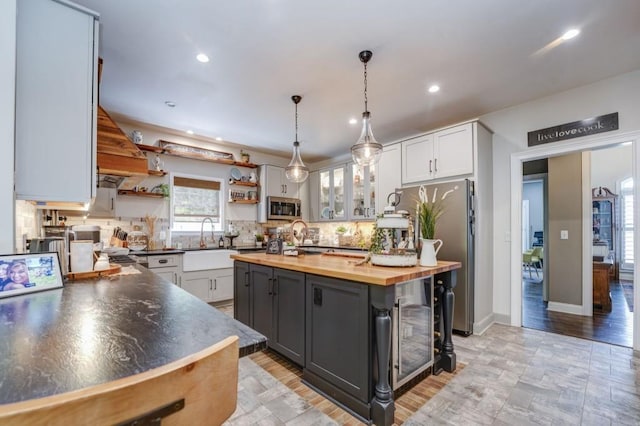 kitchen with appliances with stainless steel finishes, wood counters, white cabinetry, sink, and a center island