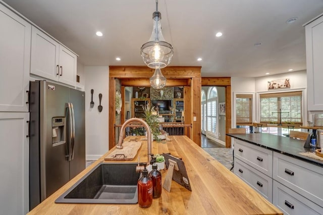 kitchen featuring decorative light fixtures, sink, white cabinets, wooden counters, and stainless steel refrigerator with ice dispenser